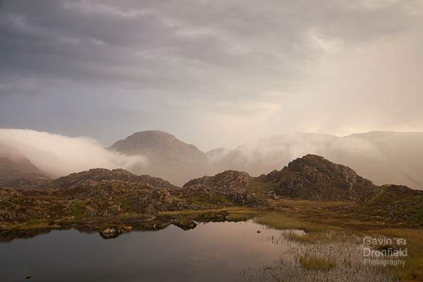 great gable above swirling clouds at sunset viewed from innominate tarn on haystacks