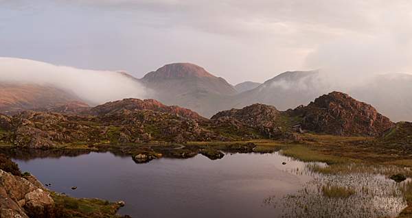 Innominate Tarn view towards red tinged Great Gable during atmospheric stormy sunset