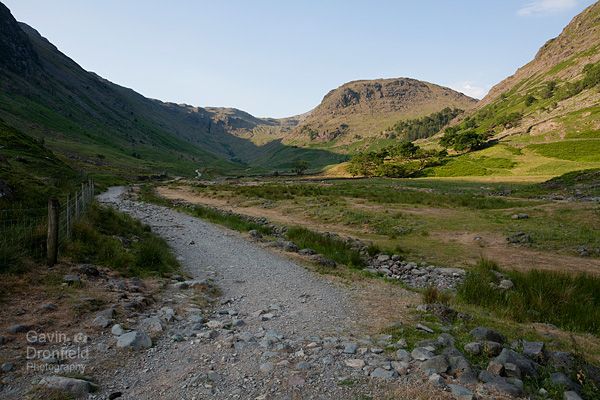 track leading from seathwaite farm towards distant seathwaite fell under blue sky with valley in shade