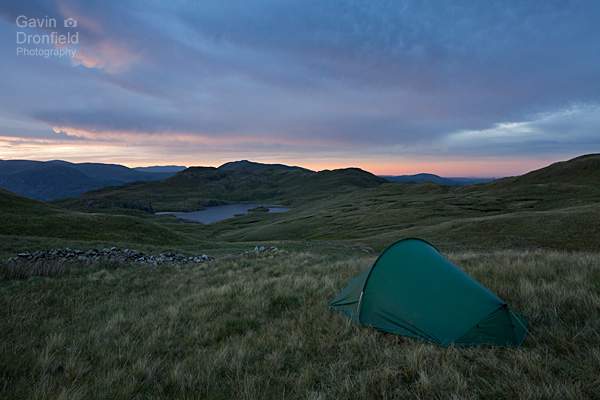 tent pitched under brock crags with view of angle tarn and angletarn pikes under colourful cloudy sunset skies