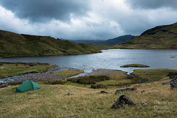 stickle tarn under stormy skies at sunset with a tent on the tarn shore