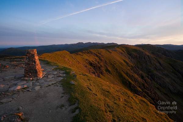 trig point on old man of coniston above ridge towards swirl how side lit red by rising sun