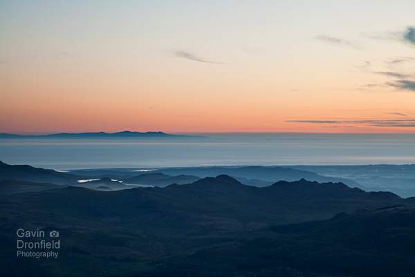 silhouetted view of green crag with distant isle of man under orange sky at dusk seen from brim fell