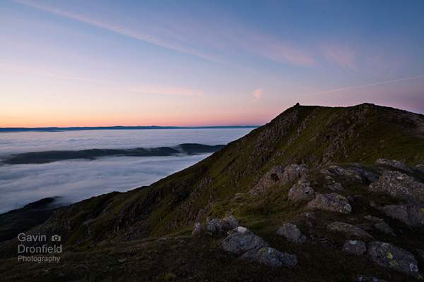 ridge to old man of coniston summit cairn above cloud inversion under colourful red blue yellow dawn sky