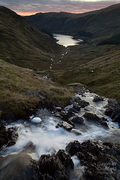 small water beck tumbles over a waterfall flowing towards distant haweswater under red dawn skies