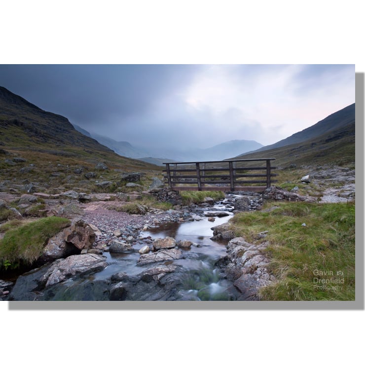 wooden footbridge over styhead gill with dark moody clouds shrouding the fells