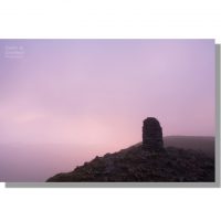 atmospheric pink tinged cloud swirling round silhouetted summit cairn on dale head at dawn