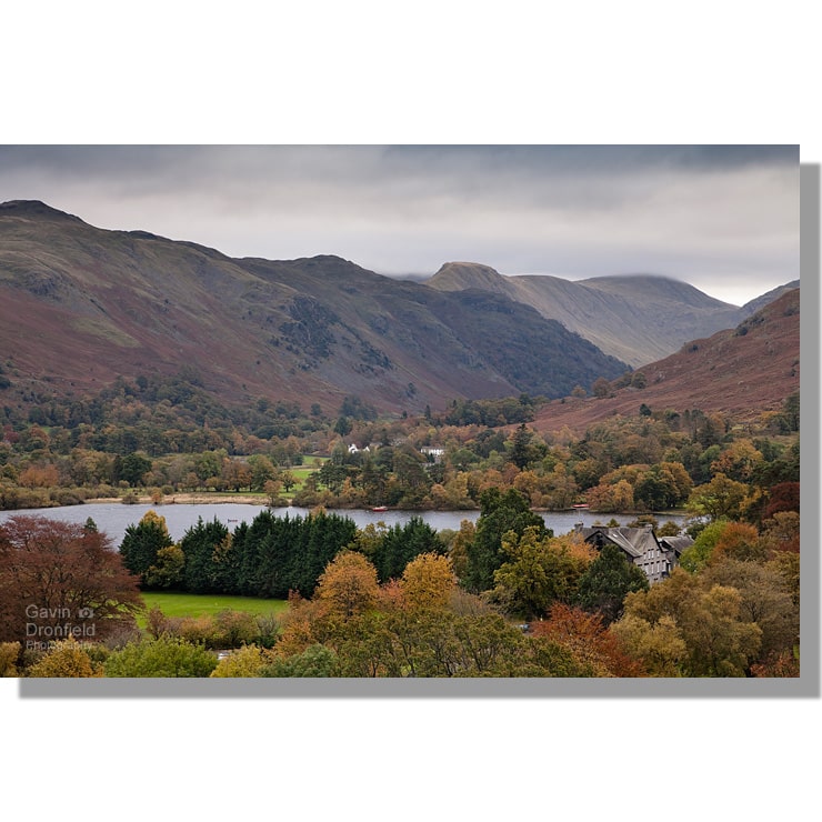 colourful autumnal trees concealing glenridding and patterdale with brock crag in background under leaden skies