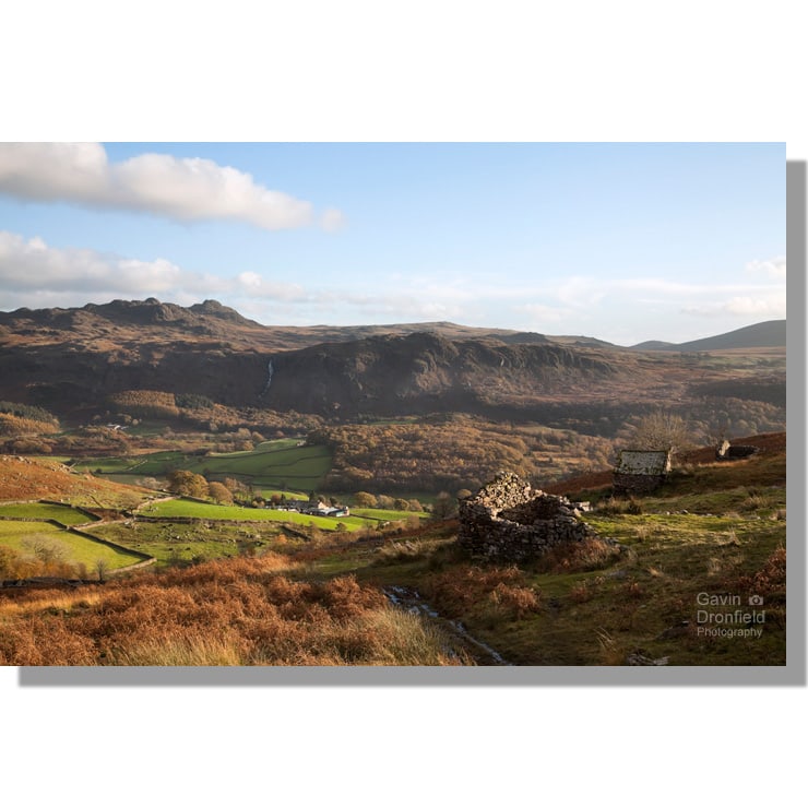 ruined peat houses atop boot bank overlooking autumnal eskdale valley under blue skies with green crag in background
