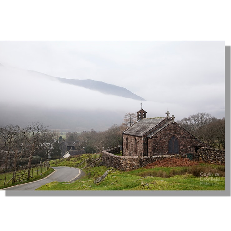 st. James church next to country lane above buttermere village on a grey autumnal morning amidst mist enshrouded fells