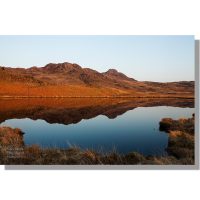green crag and crook crag reflected in calm low birker tarn bathed in red light at sunset under clear blue skies