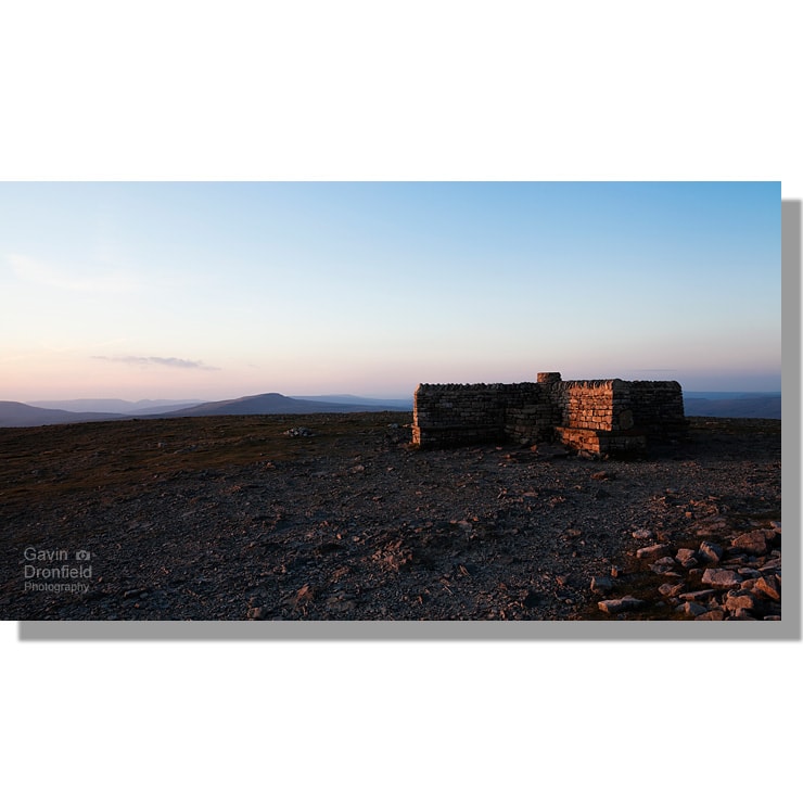 stone shelter on ingleborough summit at sunset with view of whernside under clear red blue sky